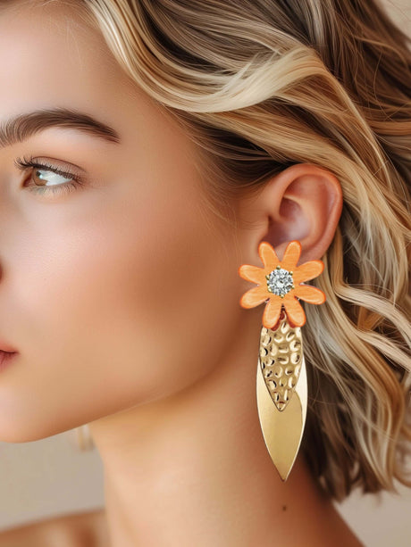 Vrouw draagt Meef oranje statement oorbel met bloem, gemaakt van messing en hars met zirkonia accenten.