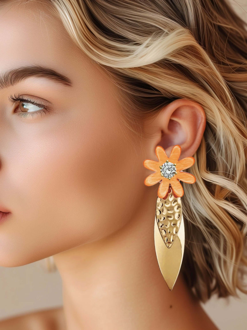 Vrouw draagt Meef oranje statement oorbel met bloem, gemaakt van messing en hars met zirkonia accenten.