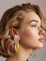 Close-up of a woman wearing Mats roze statement oorbellen met bloem, featuring pink flower design with zirkonia accents and gold details.