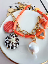 Meau bedelarmband met oranje kralen, parelhanger en gouden accenten op een stijlvolle achtergrond